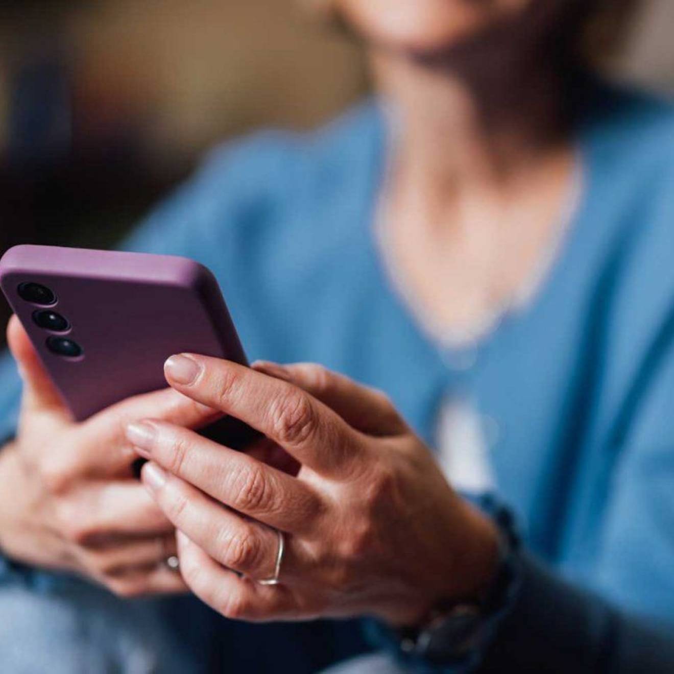 Senior woman uses smartphone; smartphone is central to image, woman's face is cropped out and body blurred