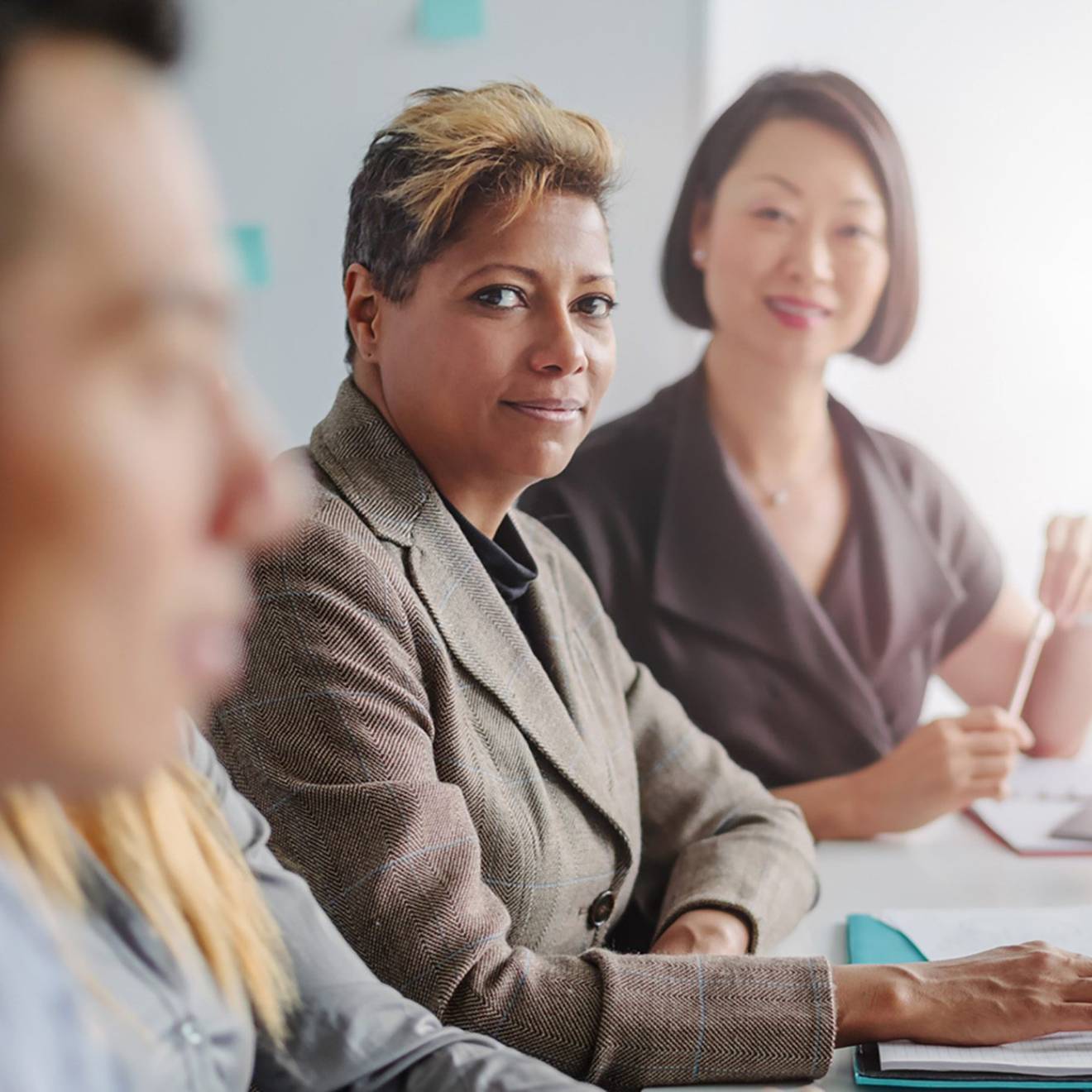 Middle-aged Black woman and middle-aged Asian woman look at a younger man in the office who is closer to the camera