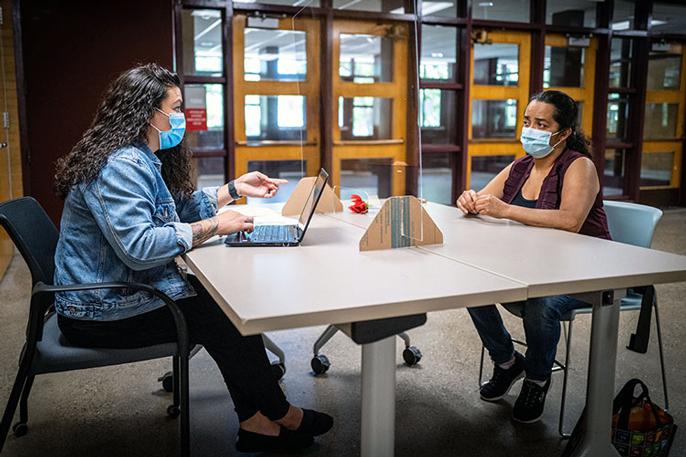 A masked teacher (left), sits at a large table with a masked mother at a school in Des Moines, Iowa, to register her child for school