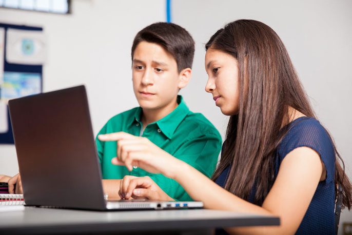 Teen helping another teen use a computer