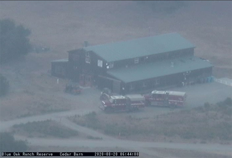 Fire trucks parked next to a barn, aerial shot