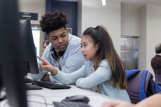 Black teenager and Asian teenager work on a computer together