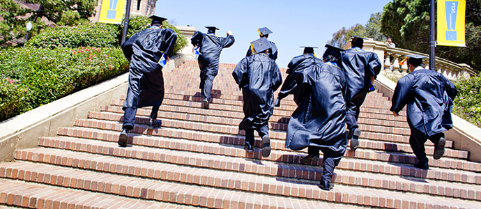 students in graduation gowns running up stairs