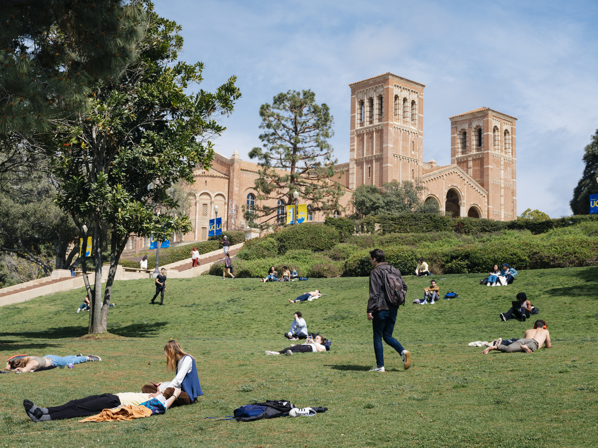 Students lounge and walk across the green on a sunny day at the UCLA campus; Royce Hall in the background