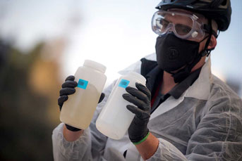 Man in PPE holds wastewater samples