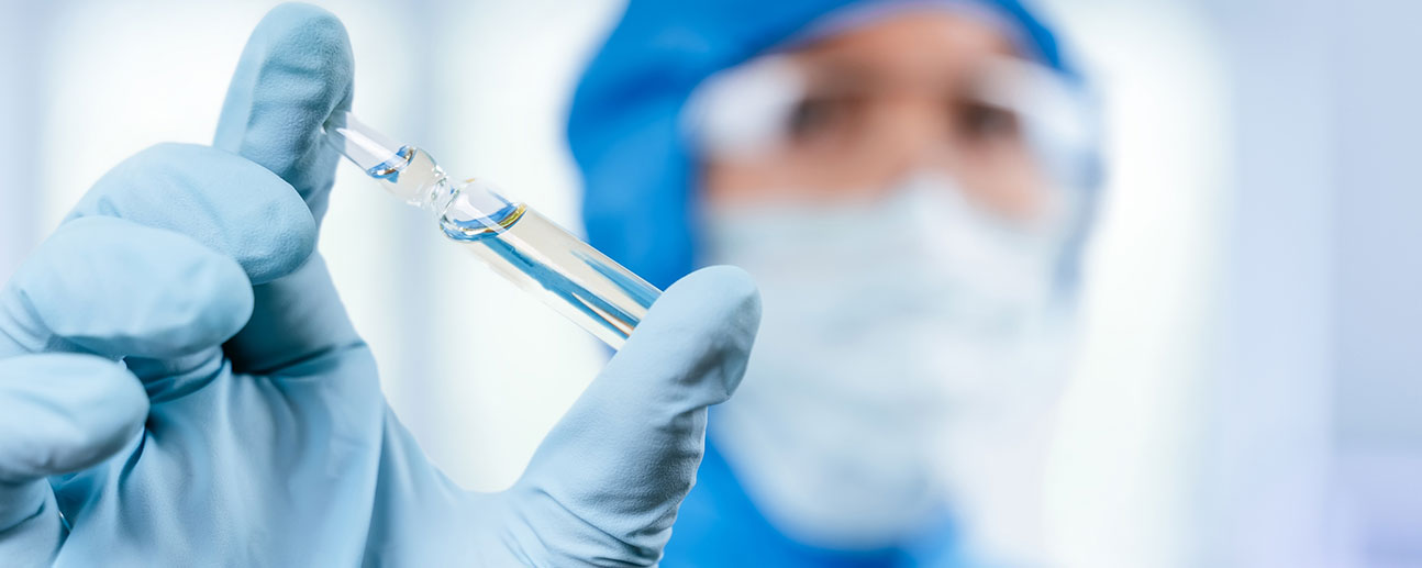 person in medical gear holding a vaccine