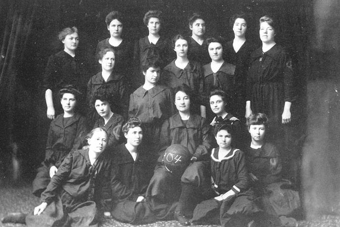 Women wearing black uniforms pose with a basketball